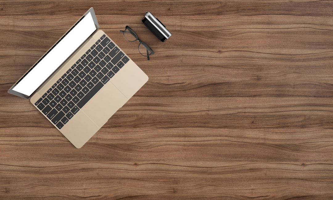 A laptop with a blank screen, glasses, and a small case on a wooden desk