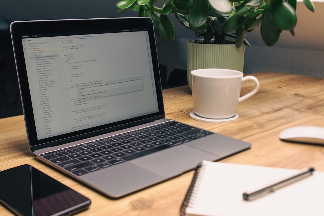 Laptop, notebook, phone, and mug on desk.